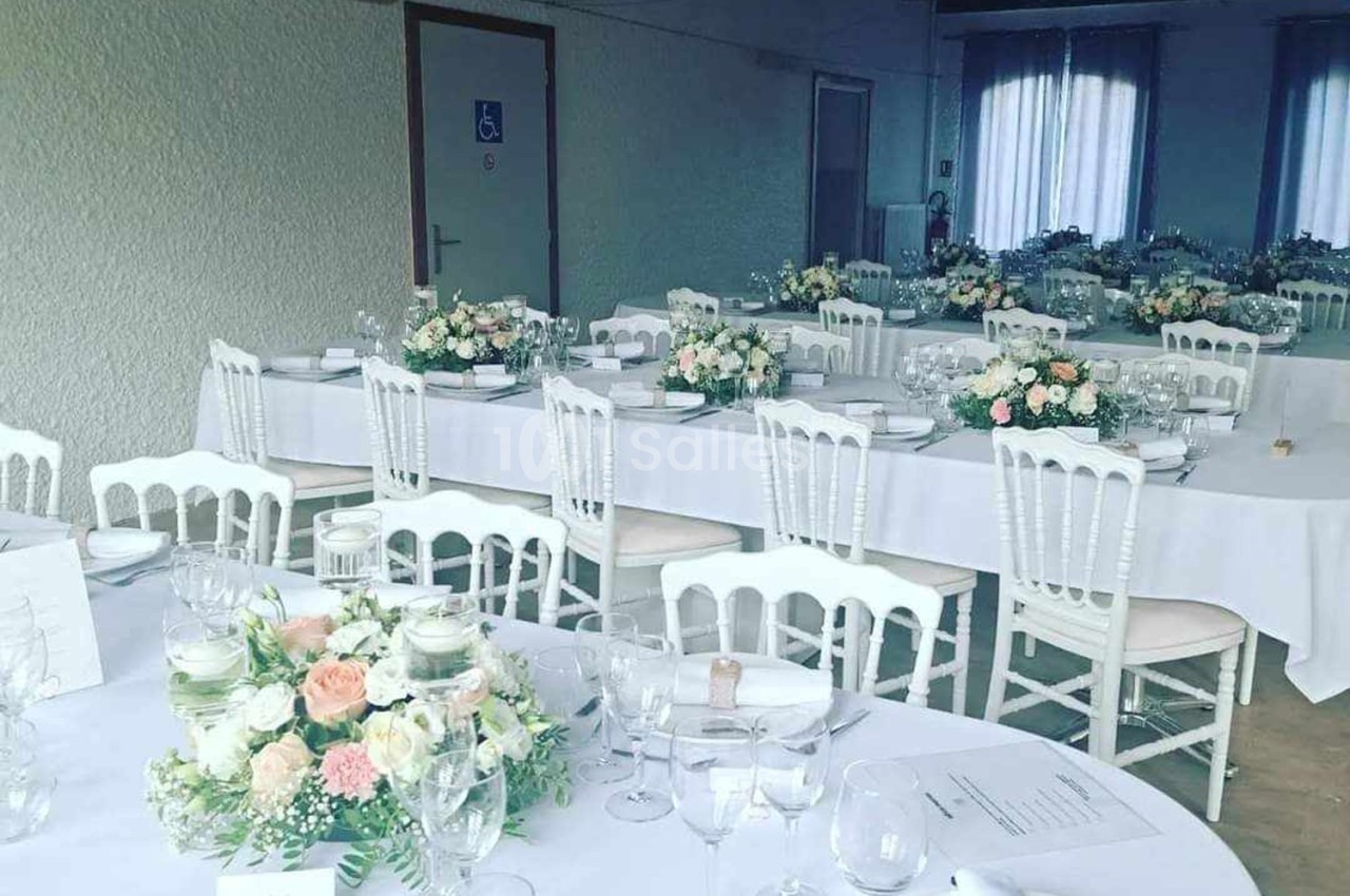Salle de réception décorée avec des tables blanches, des chaises assorties et des compositions florales pastel.