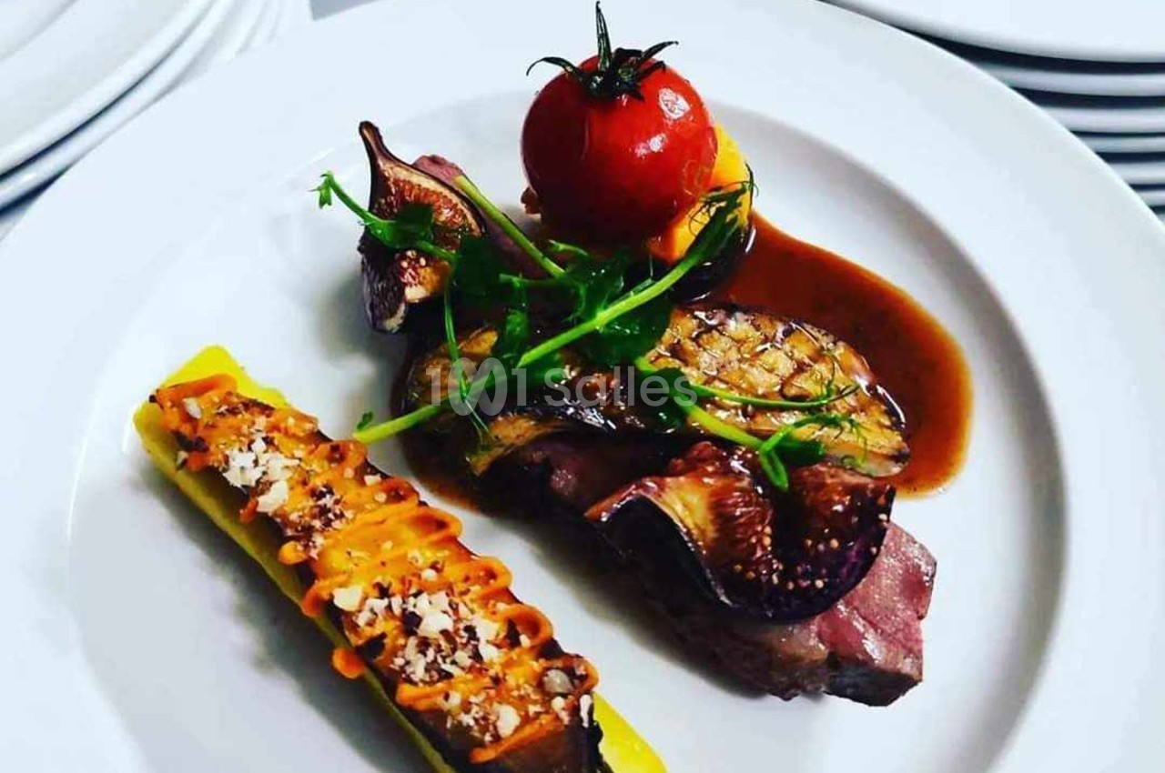 Assiette gastronomique avec viande, figues, tomate rôtie, courgette garnie et sauce, présentée sur une assiette blanche.