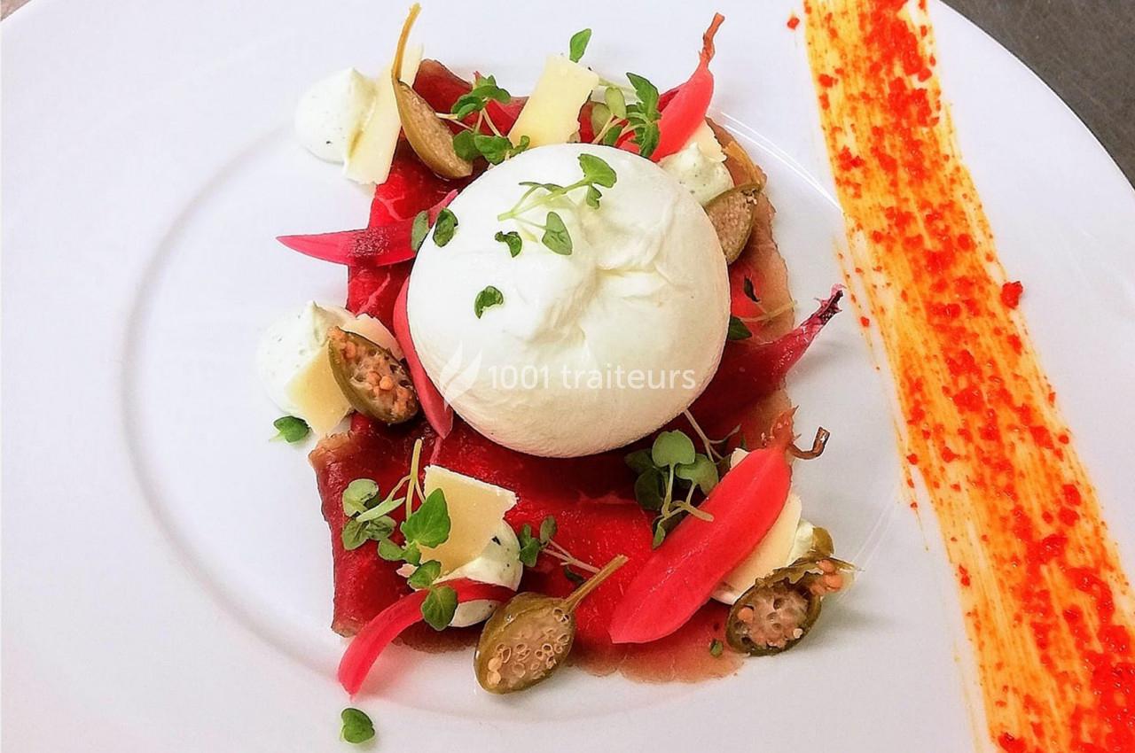 Assiette de burrata avec légumes marinés, copeaux de fromage, câpres et touche de sauce colorée sur le côté.