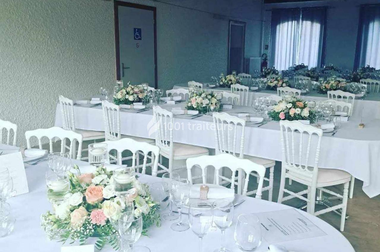 Salle de réception décorée avec des tables blanches, des chaises assorties et des compositions florales pastel.