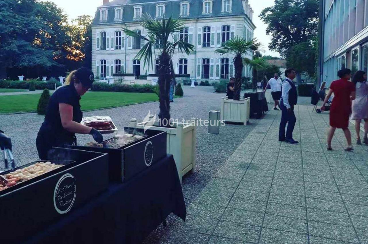 Serveuse préparant un buffet en plein air devant un bâtiment historique entouré de palmiers et d'espaces verts.