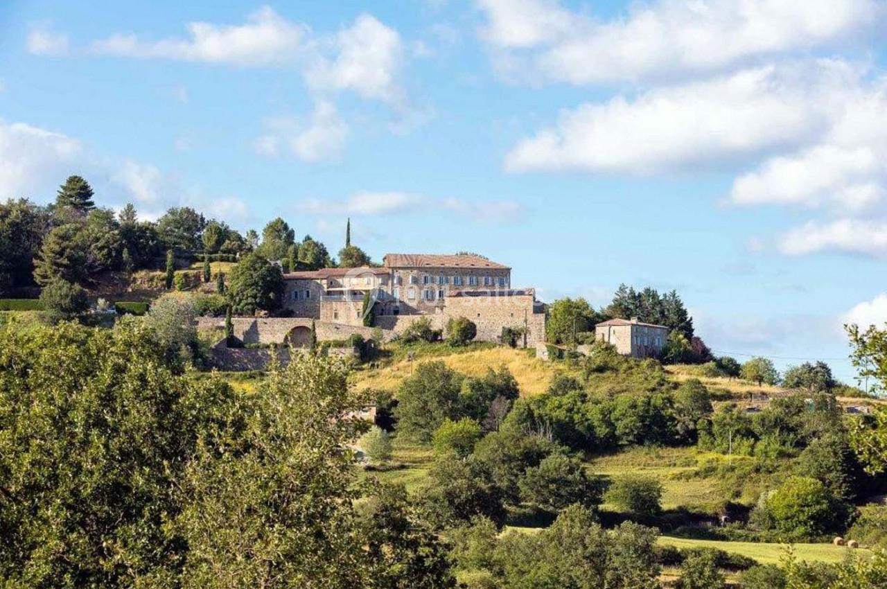 Vue d'un village perché avec des bâtiments en pierre entourés de végétation sous un ciel partiellement nuageux.