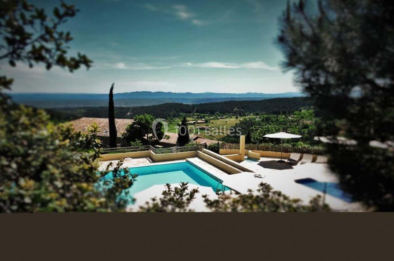 Vue d'une piscine entourée de végétation, avec un paysage vallonné et ensoleillé à l'arrière-plan.