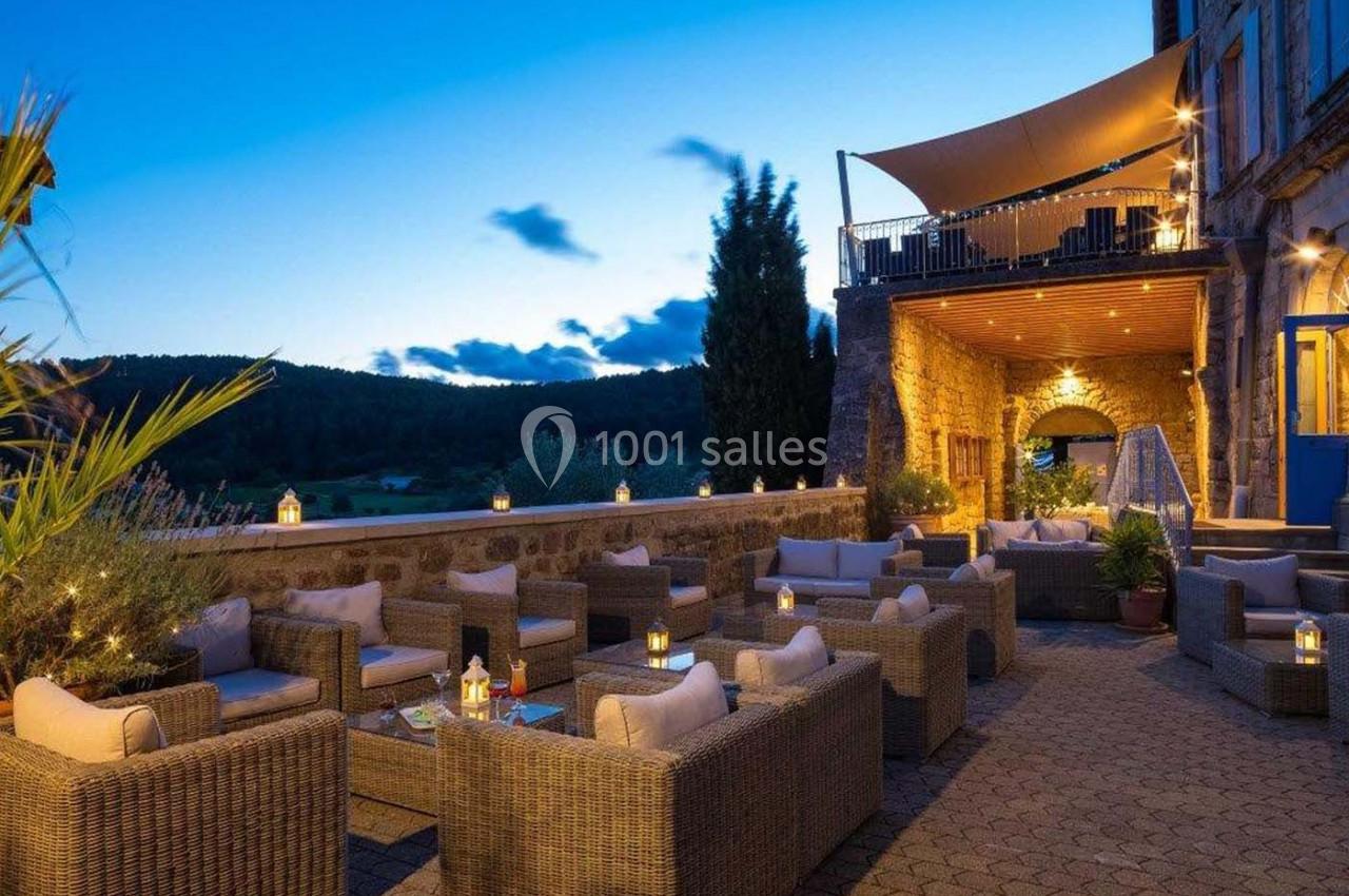 Terrasse extérieure aménagée avec des fauteuils en rotin, éclairée par des lanternes au crépuscule.