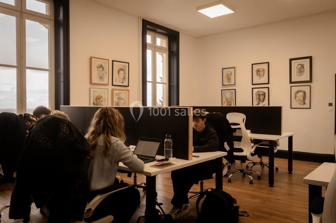 Personnes travaillant sur des ordinateurs dans un espace de coworking lumineux avec des portraits accrochés aux murs.