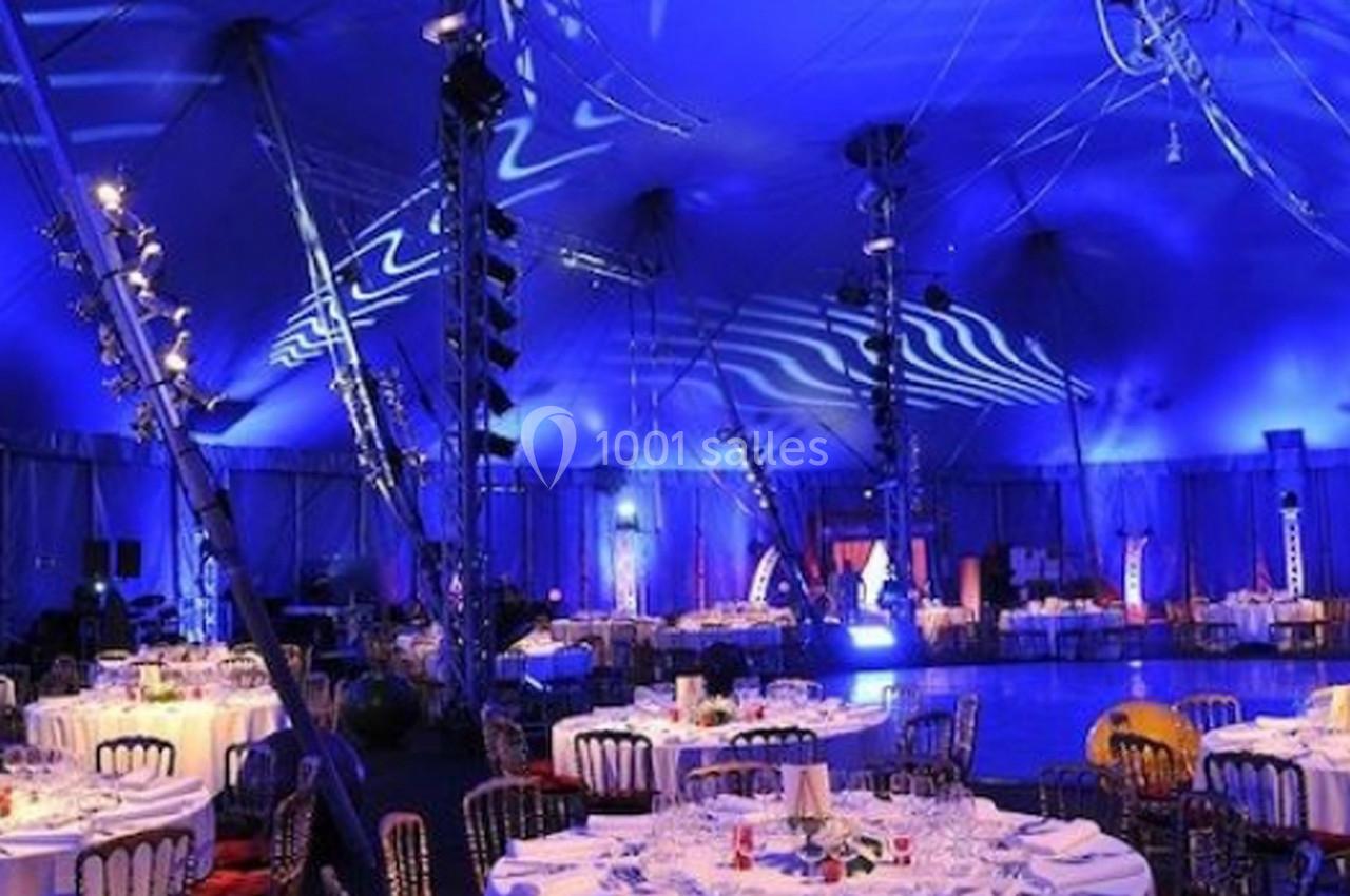 Salle de réception sous un chapiteau éclairé en bleu, avec tables dressées et décorations festives.