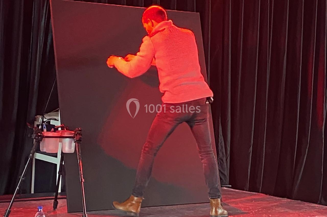 Un homme debout peint ou travaille sur une grande toile noire dans un environnement éclairé en rouge.