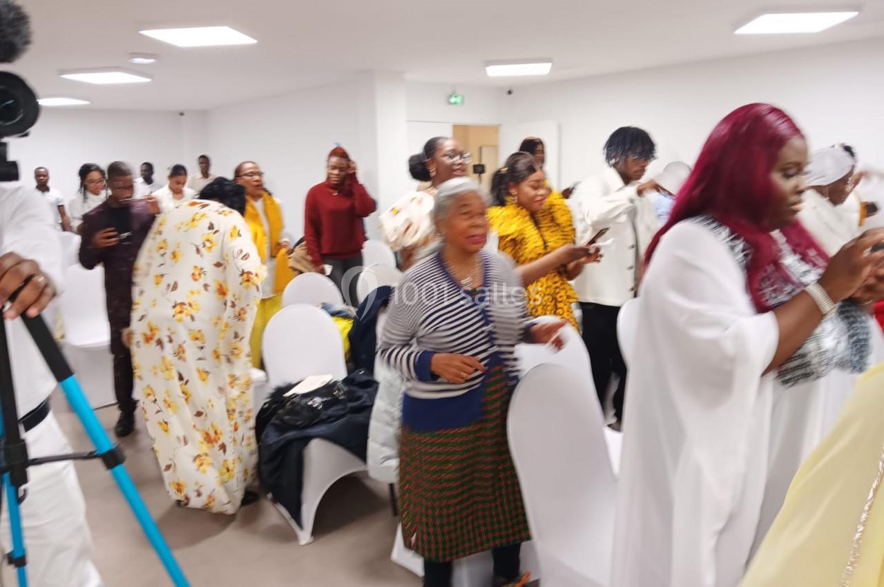 Des personnes debout dans une salle blanche, certaines en tenue colorée, semblant participer à un événement collectif.