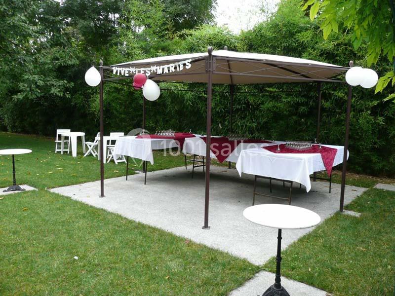 Tente de réception décorée avec des nappes rouges et blanches, installée dans un jardin verdoyant.