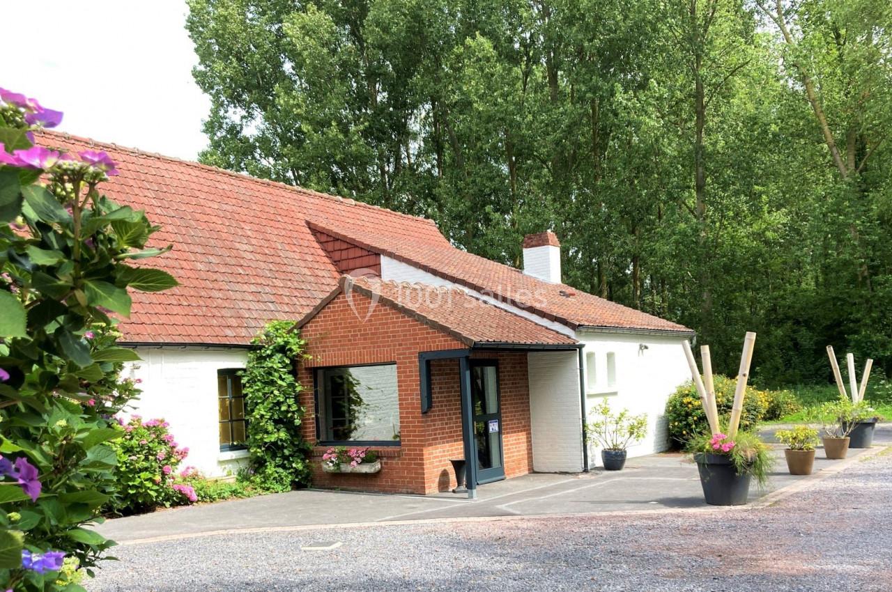 Maison en briques et crépi blanc avec toit en tuiles rouges, entourée de plantes et d'arbres verdoyants.