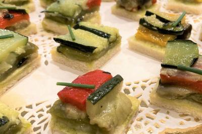 Homme concentré cuisinant en extérieur sur une plancha, entouré de végétation sous un ciel nuageux.