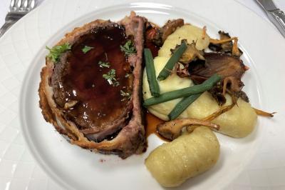 Homme concentré cuisinant en extérieur sur une plancha, entouré de végétation sous un ciel nuageux.