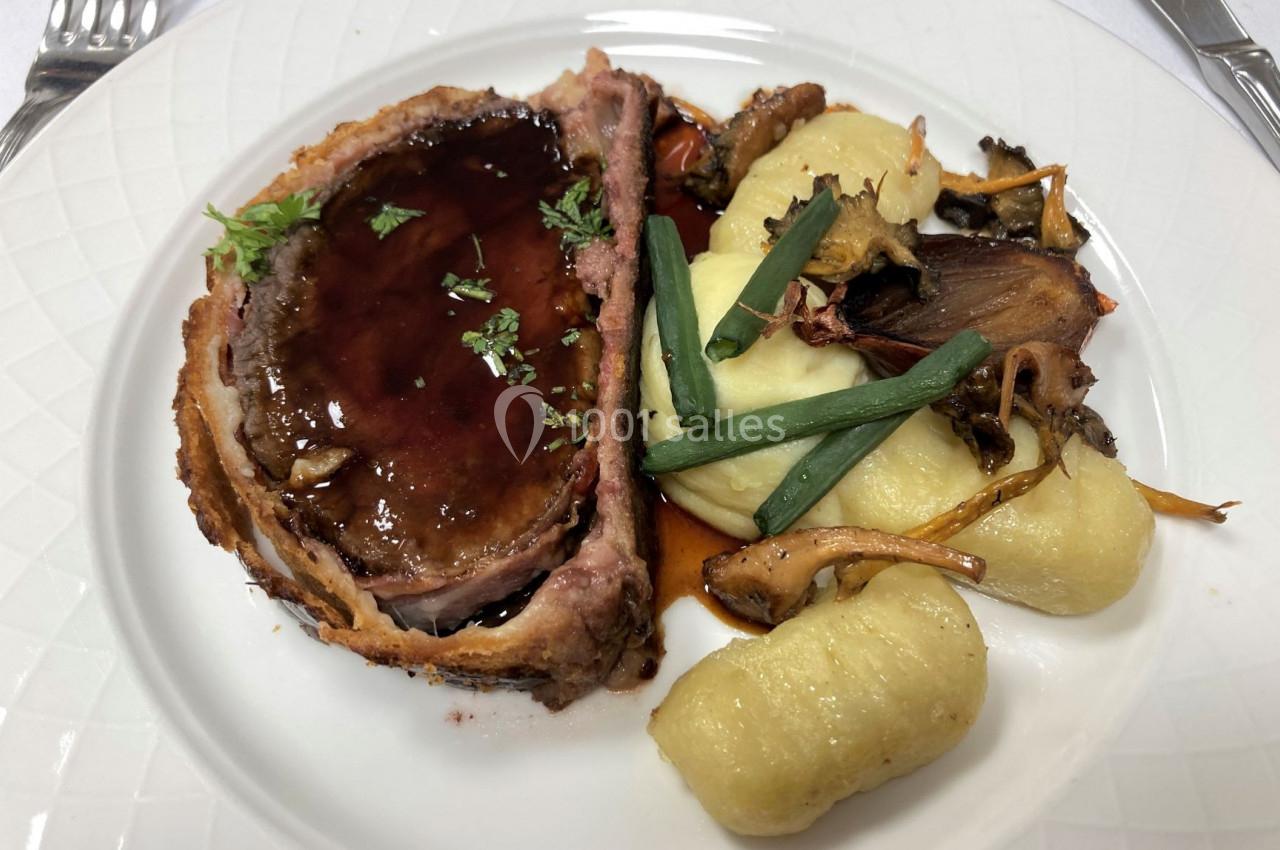 Assiette contenant un filet de viande en croûte avec sauce, gnocchis, champignons et légumes verts.