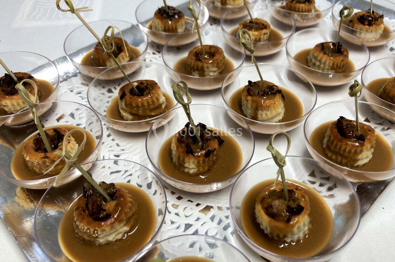 Bouchées apéritives disposées sur un plateau, composées de vol-au-vent garnis de sauce et décorés de brochettes.