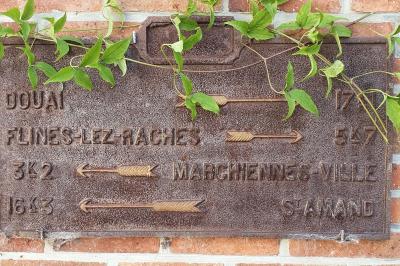 Homme concentré cuisinant en extérieur sur une plancha, entouré de végétation sous un ciel nuageux.