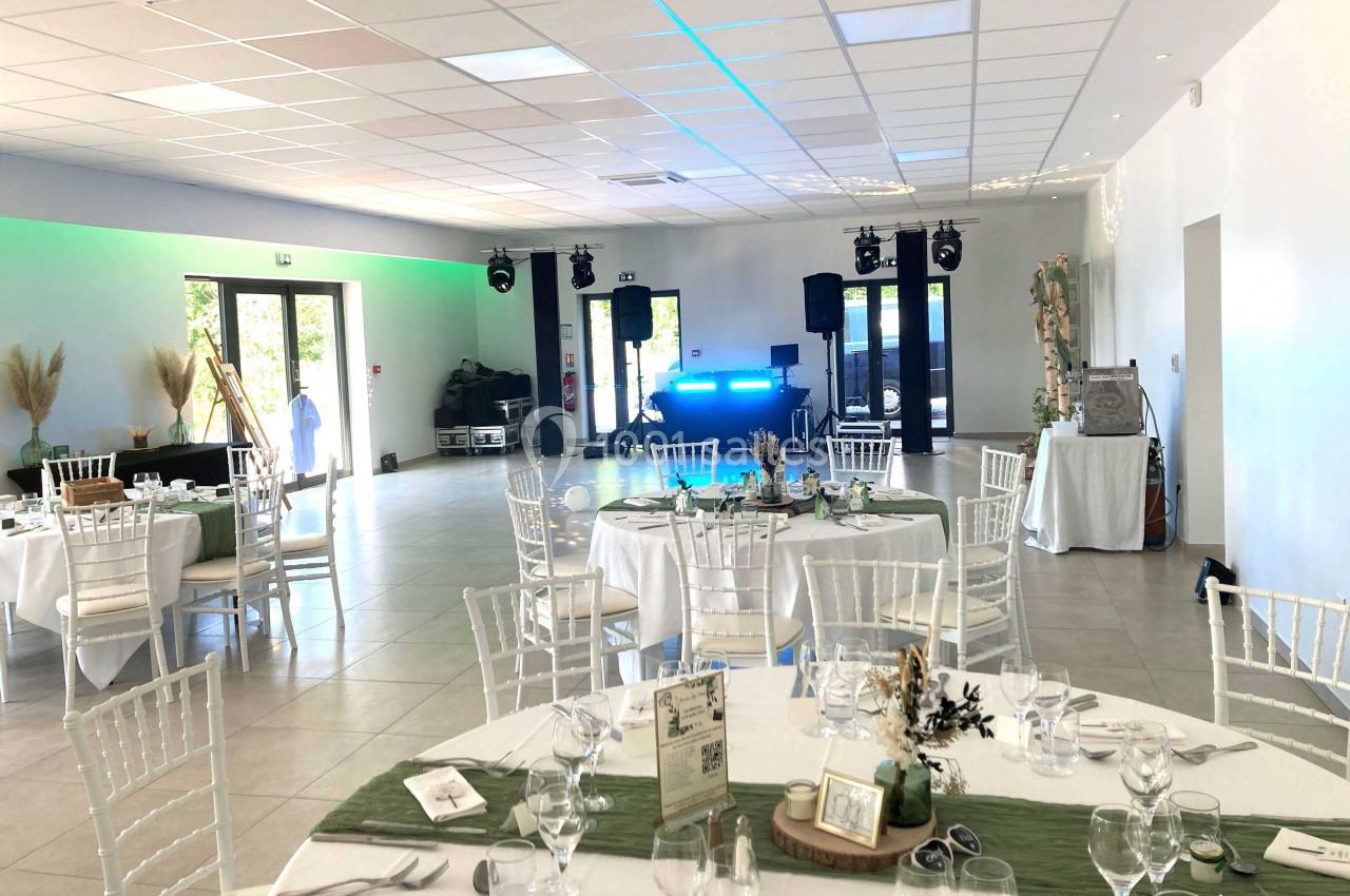 Salle de réception lumineuse avec tables dressées, chaises blanches et espace pour une piste de danse équipée de matériel…