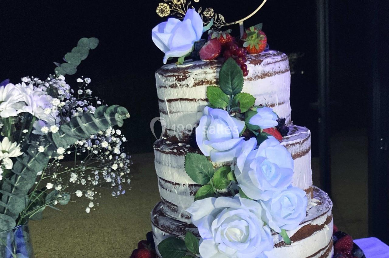 Gâteau de mariage à trois étages décoré de roses blanches, fruits rouges et un topper personnalisé.