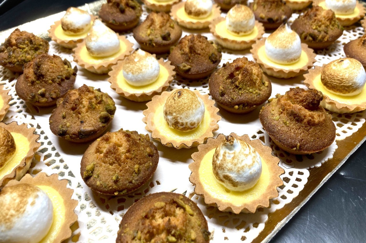 Assortiment de mini-tartelettes garnies de meringue dorée et de petits gâteaux aux éclats de pistache.