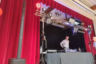 Un DJ mixe dans une salle éclairée par des lumières colorées, avec des tables hautes et un décor sobre.