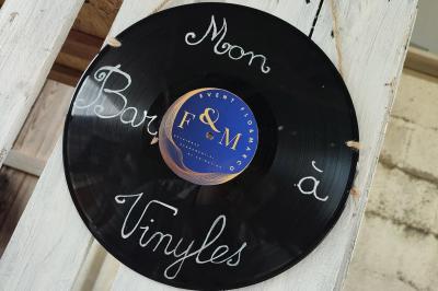 Un DJ mixe dans une salle éclairée par des lumières colorées, avec des tables hautes et un décor sobre.