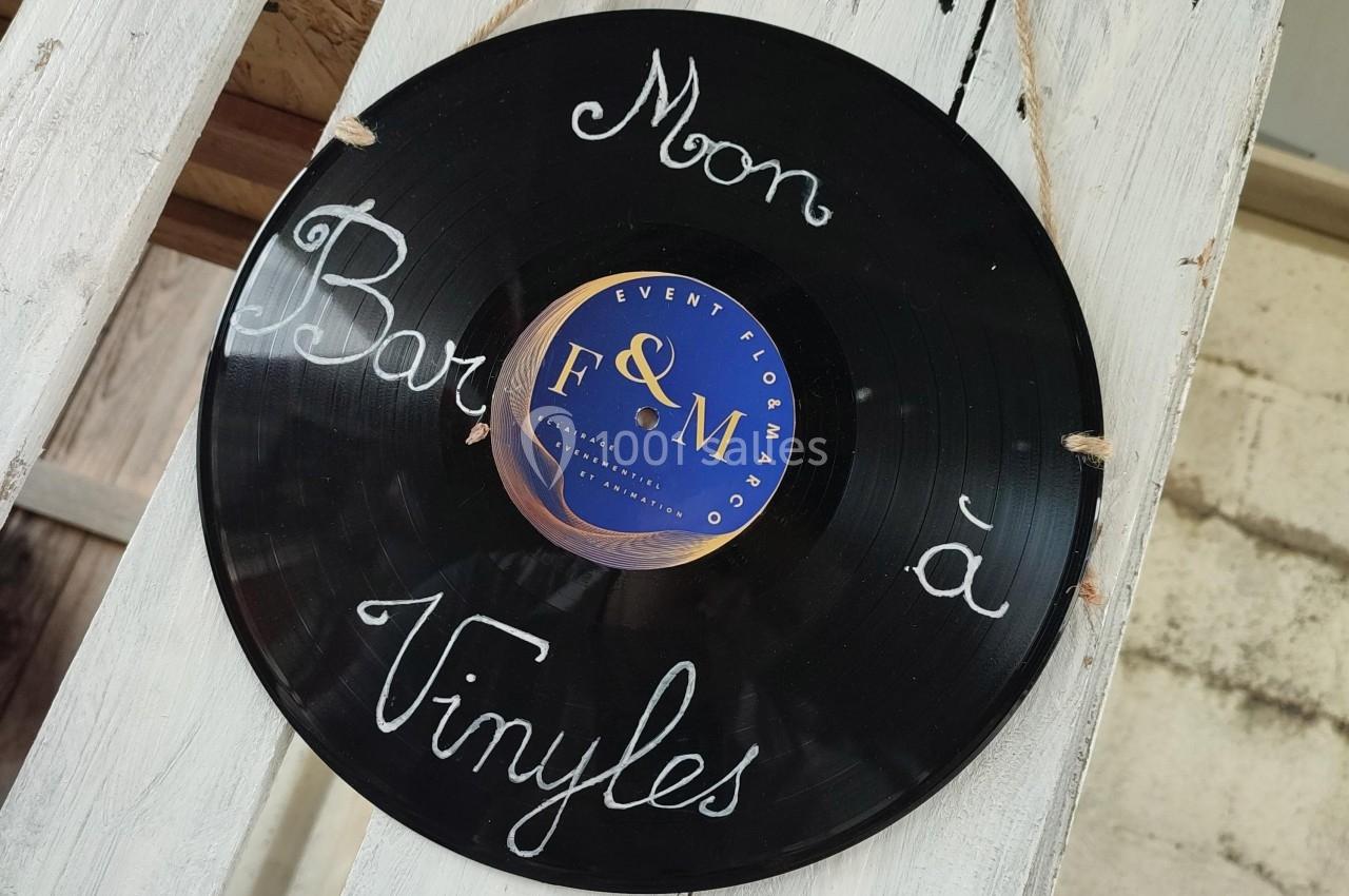 Disque vinyle noir suspendu avec l'inscription manuscrite ’Mon bar à vinyles’ sur un fond en bois clair.