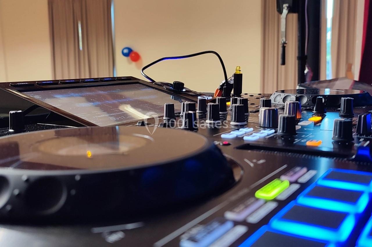 Table de mixage avec platine, boutons et écran tactile, installée dans une salle éclairée avec rideaux et ballons en arrière…