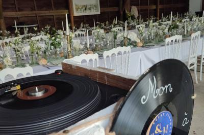 Un DJ mixe dans une salle éclairée par des lumières colorées, avec des tables hautes et un décor sobre.