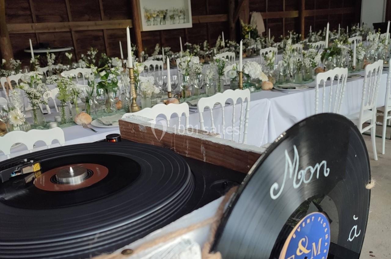 Salle de réception décorée pour un mariage, avec des tables ornées de fleurs et un tourne-disque en premier plan.