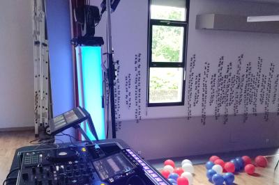 Un DJ mixe dans une salle éclairée par des lumières colorées, avec des tables hautes et un décor sobre.