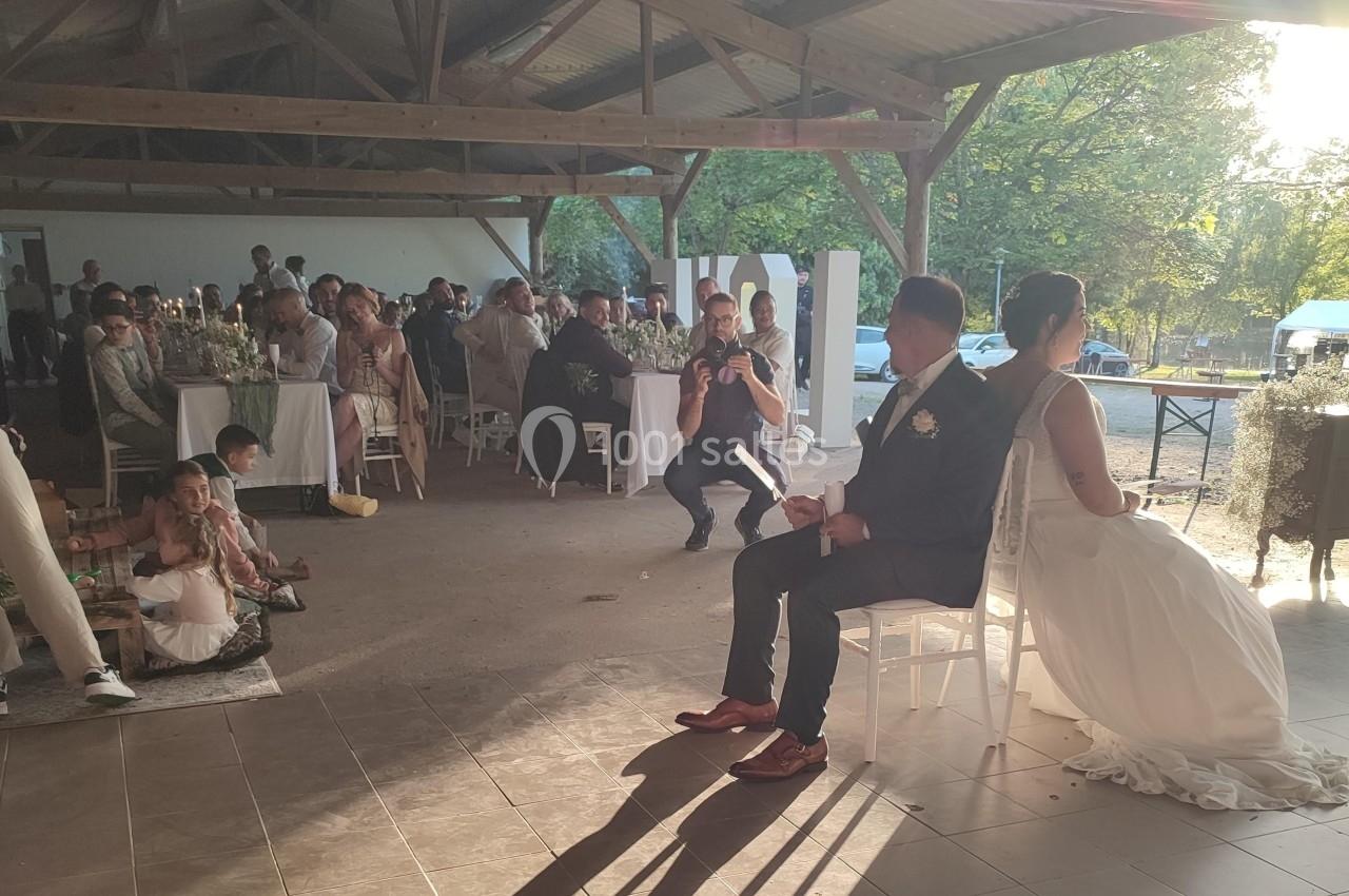 Un couple assis lors d'une cérémonie dans une salle ouverte, entouré d'invités et baigné par une lumière naturelle.
