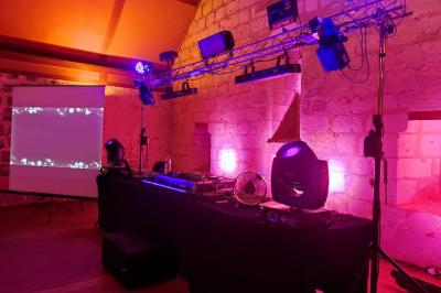 Un DJ mixe dans une salle éclairée par des lumières colorées, avec des tables hautes et un décor sobre.