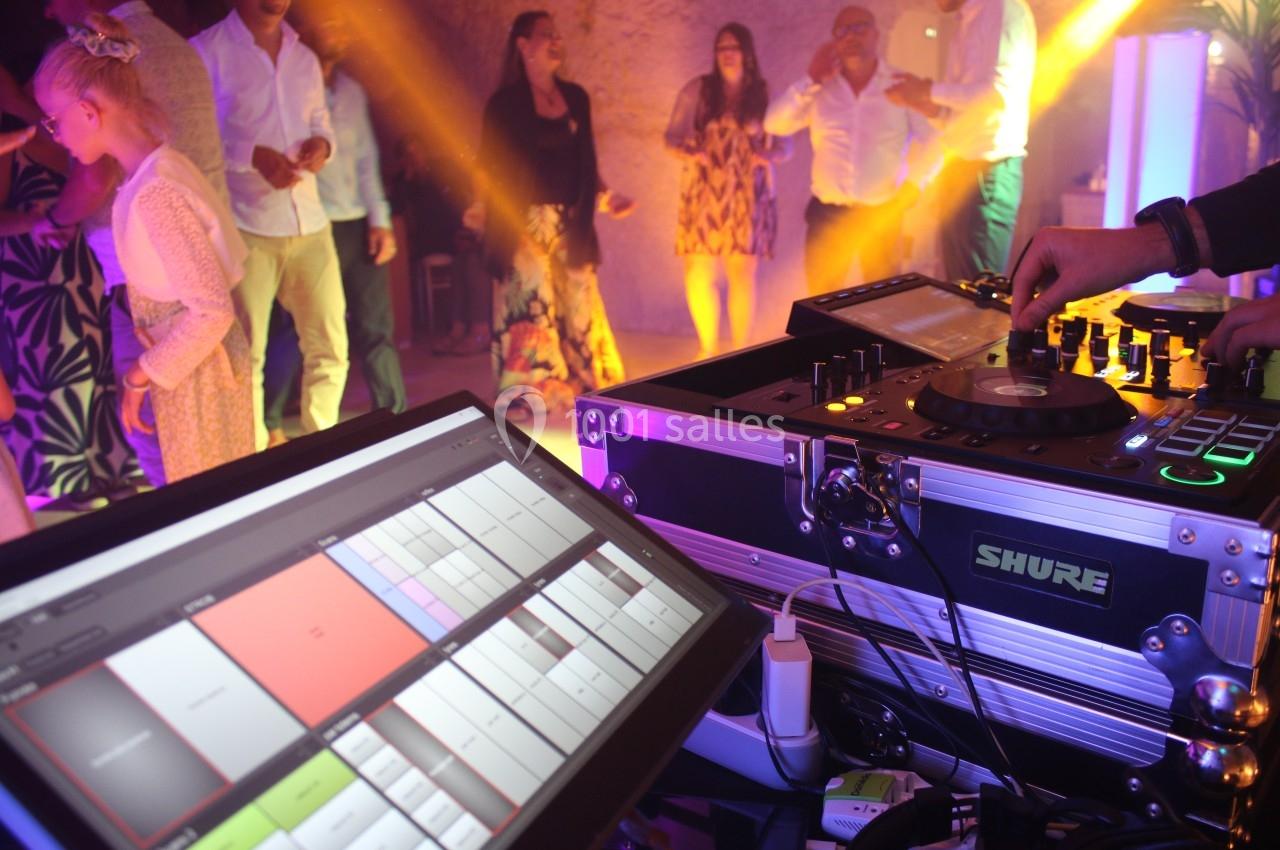 Vue d'une table de mixage et d'un écran de contrôle lors d'une soirée dansante avec des invités en arrière-plan.