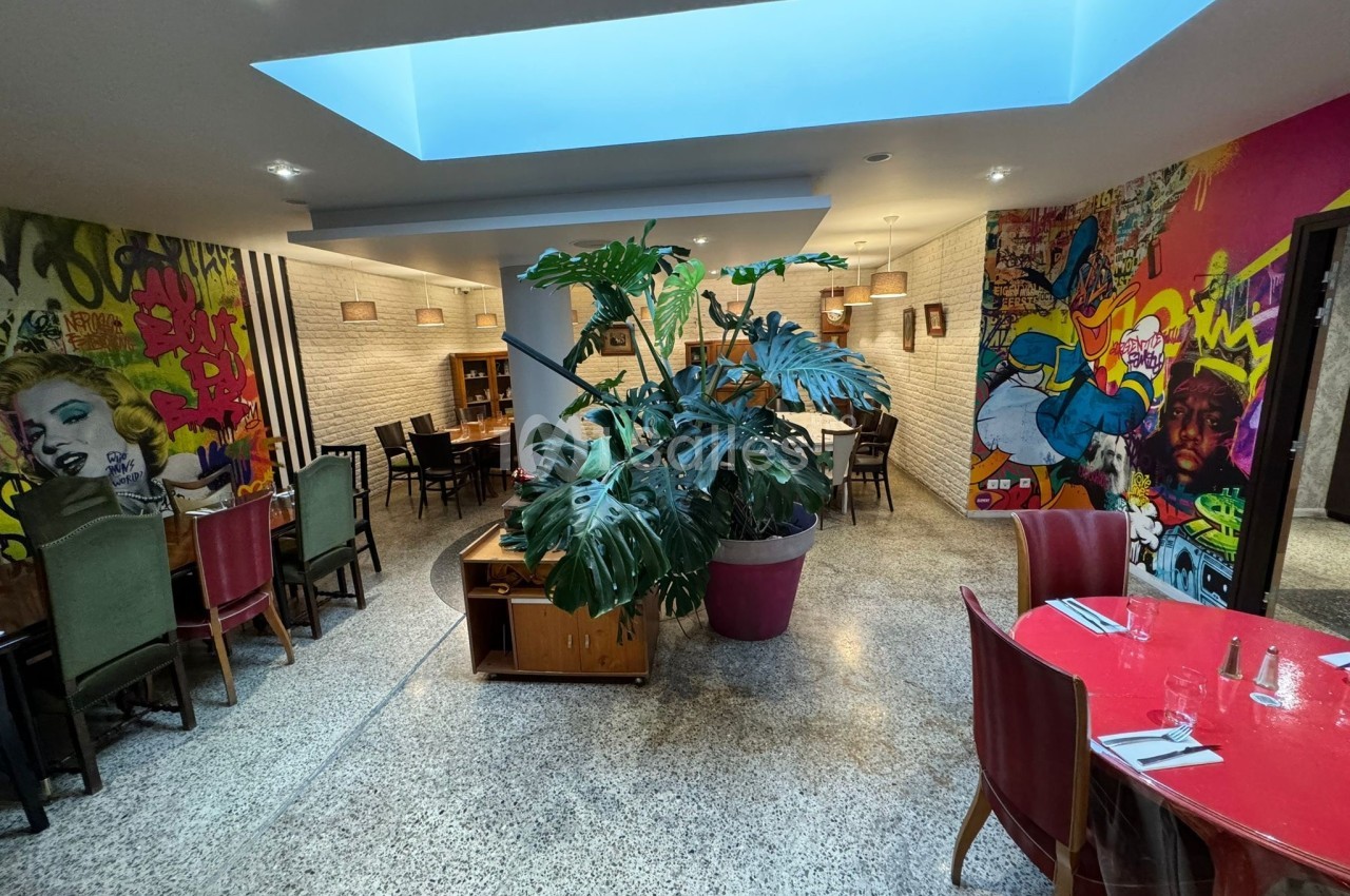 Salle de restaurant moderne avec fresques murales colorées, mobilier varié et grande plante en pot au centre.