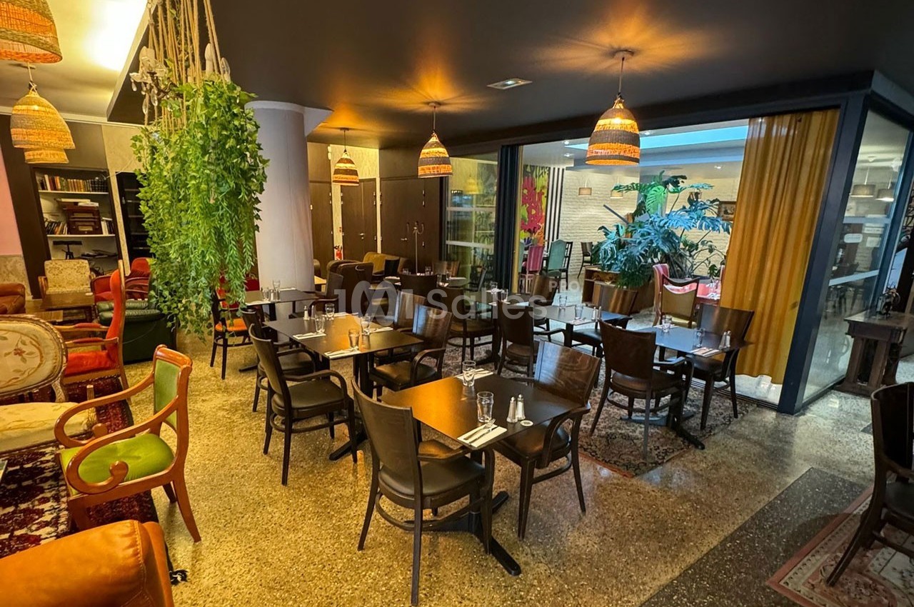 Salle de restaurant chaleureuse avec tables en bois, chaises assorties, luminaires suspendus et plantes décoratives.