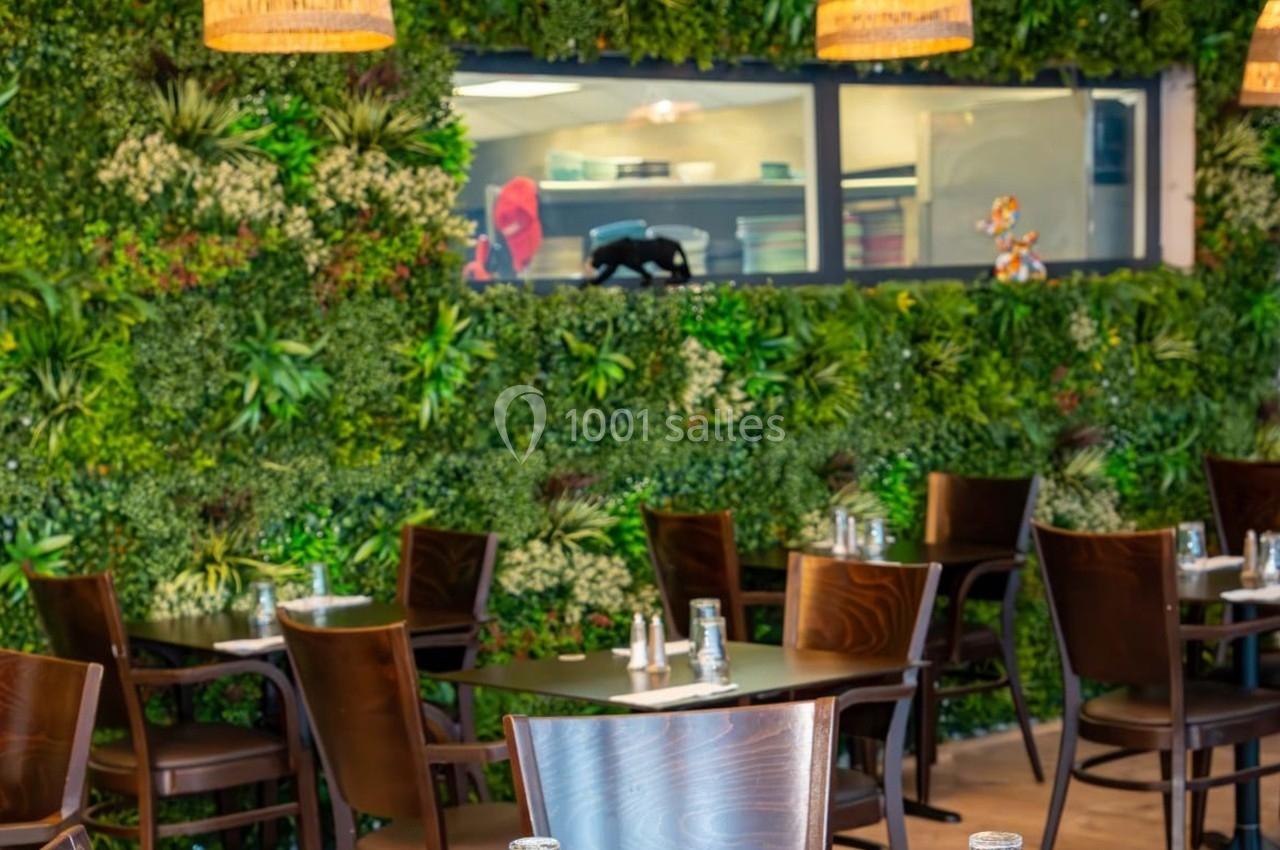 Salle de restaurant avec tables en bois, chaises assorties et mur végétal décoratif en arrière-plan.