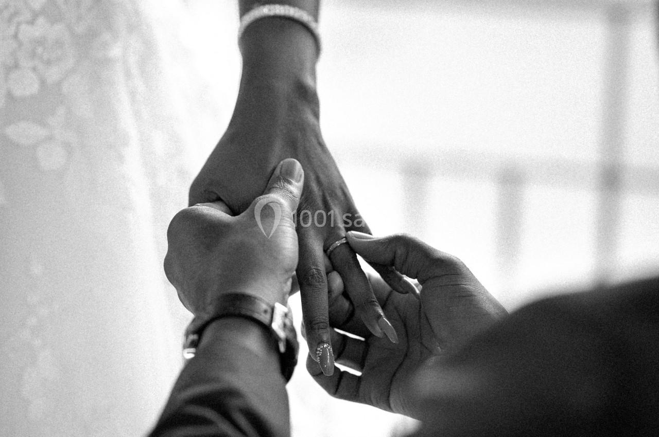 Un homme glisse une bague au doigt d'une femme en robe de mariée, capturé en noir et blanc.