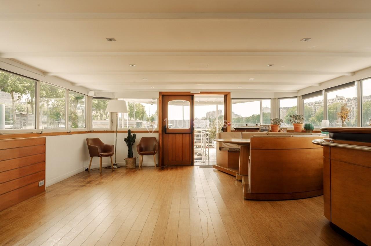 Intérieur lumineux avec parquet, mobilier en bois, grandes fenêtres et vue sur un espace extérieur.