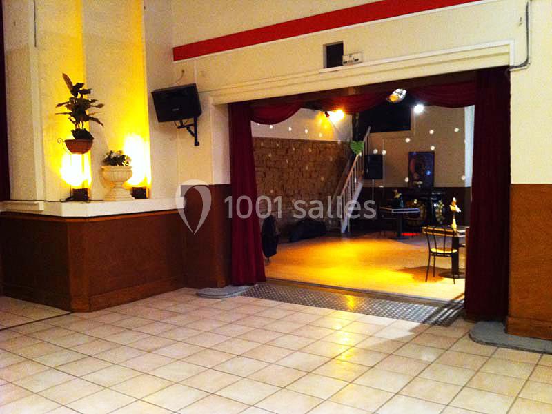 Salle avec carrelage clair, rideaux rouges ouverts dévoilant un espace avec scène, tables et éclairage tamisé.