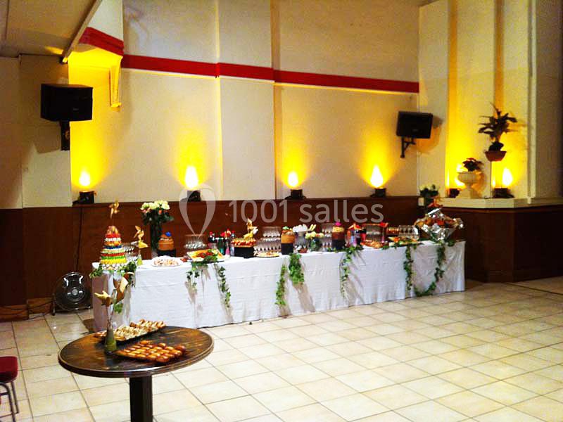 Table décorée avec nappes blanches, garnie de desserts variés, dans une salle éclairée par des lumières chaudes.