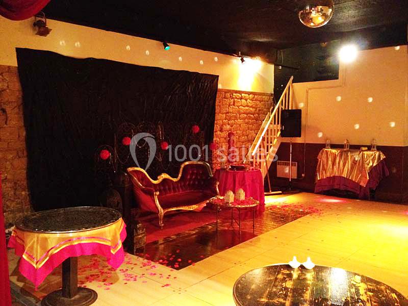 Salle décorée avec un canapé rouge, des tables ornées de nappes roses et un éclairage tamisé.