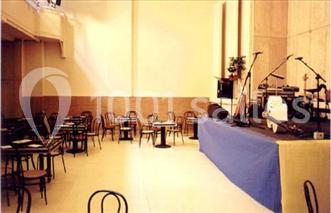 Salle avec des tables et chaises vides, une scène équipée d'instruments de musique et un éclairage naturel.
