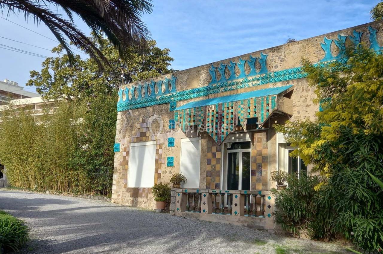 Façade d'une maison ornée de mosaïques colorées et de motifs géométriques, entourée de végétation.