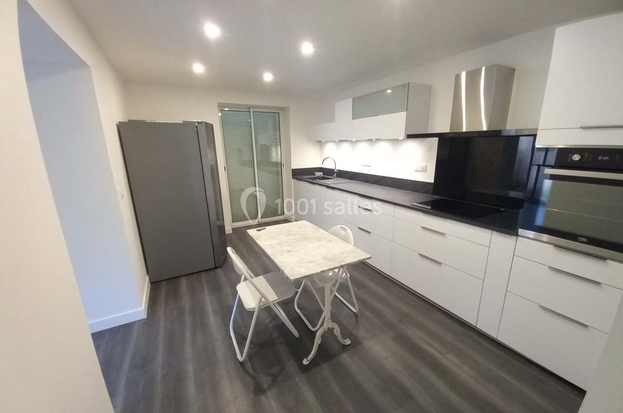 Cuisine moderne avec meubles blancs, plan de travail noir, table en marbre, chaises blanches et électroménagers intégrés.