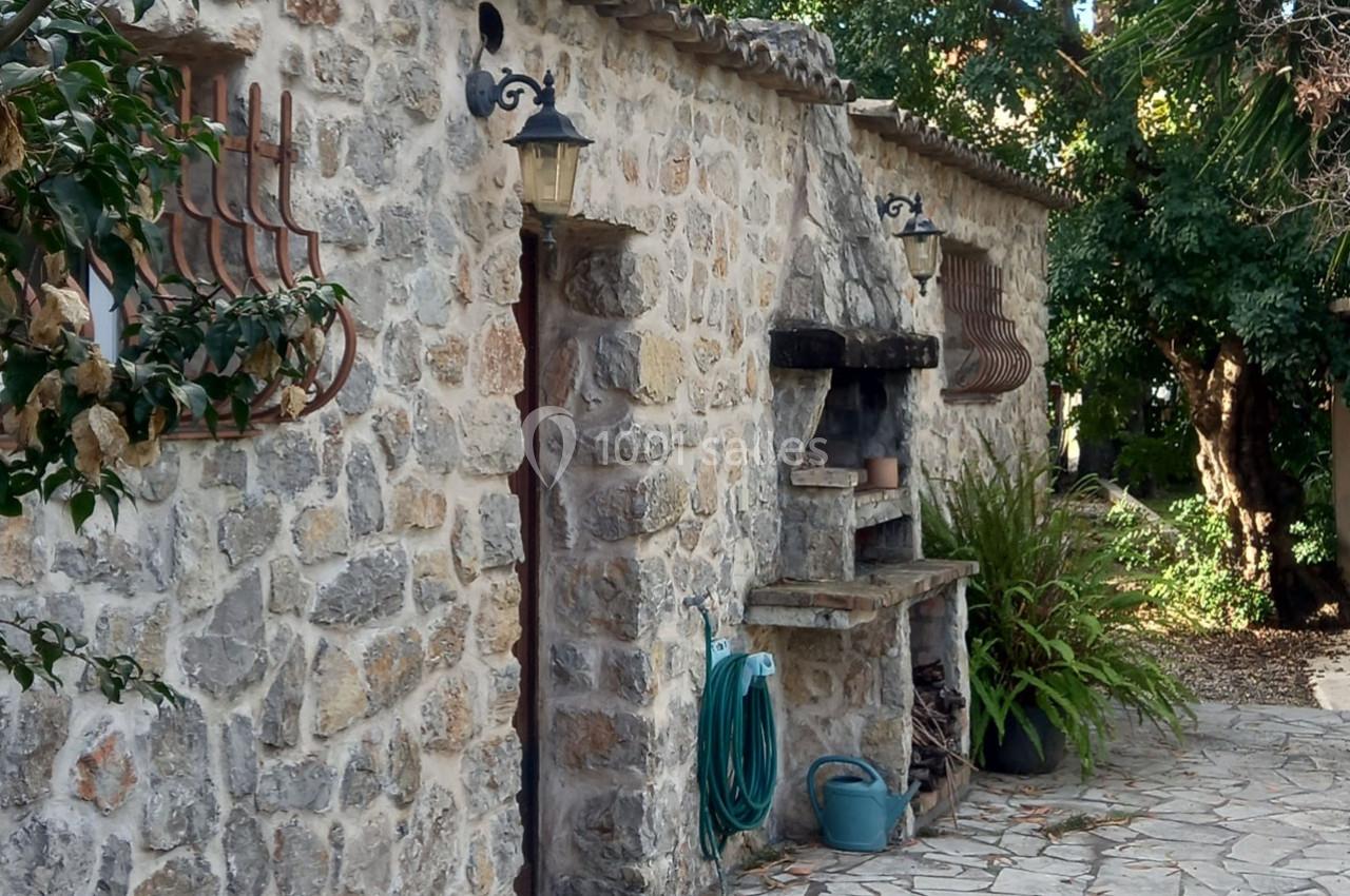Façade en pierre d'une maison avec des lanternes, un espace de rangement extérieur et des plantes sur une terrasse pavée.