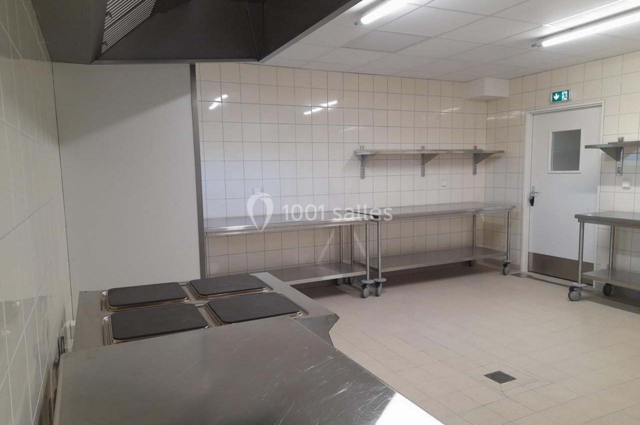 Cuisine professionnelle vide avec plans de travail en inox, carrelage mural blanc et éclairage fluorescent.