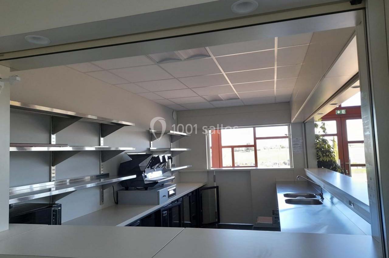 Cuisine professionnelle moderne avec plans de travail en inox, étagères murales et grandes fenêtres laissant entrer la…