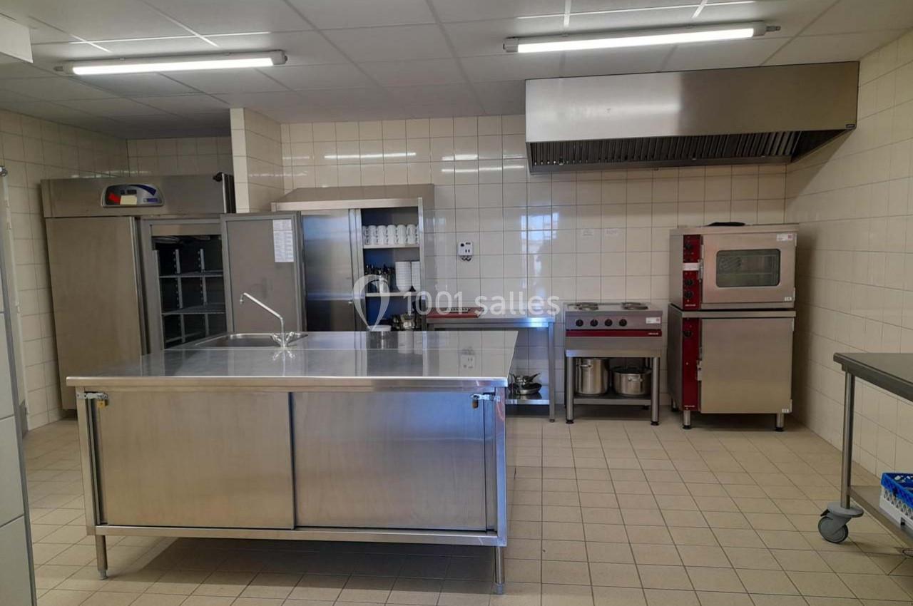 Cuisine professionnelle avec plan de travail en inox, four, plaques de cuisson, étagères et carrelage mural beige.