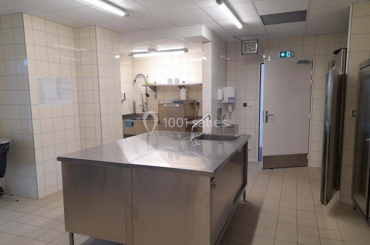 Cuisine professionnelle avec surfaces en inox, carrelage mural blanc, équipements de lavage et éclairage fluorescent.
