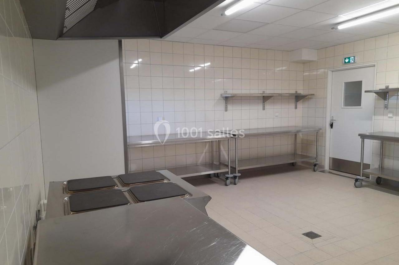 Cuisine professionnelle vide avec plans de travail en inox, murs carrelés blancs et éclairage fluorescent.