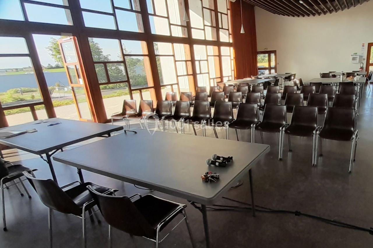 Salle de réunion lumineuse avec des rangées de chaises alignées et deux tables équipées d'accessoires.